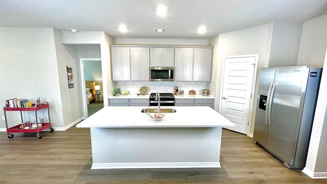 kitchen with decorative backsplash, appliances with stainless steel finishes, a kitchen island with sink, and sink