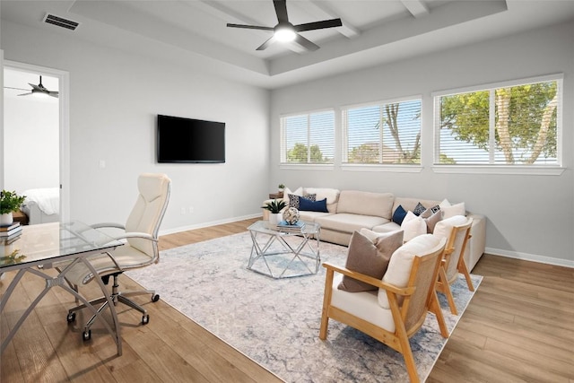 living room with ceiling fan, a raised ceiling, and light wood-type flooring