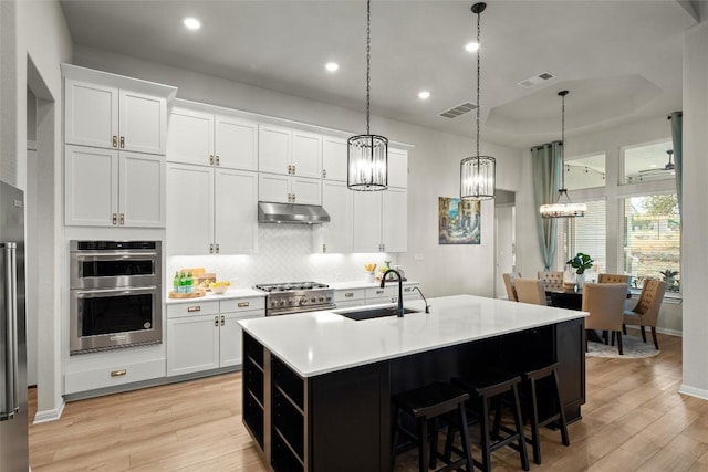 kitchen featuring appliances with stainless steel finishes, sink, white cabinetry, hanging light fixtures, and an island with sink