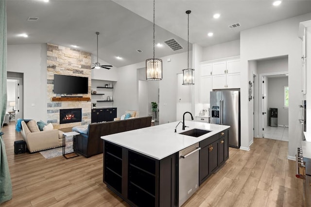 kitchen with white cabinetry, sink, stainless steel appliances, a kitchen island with sink, and a fireplace