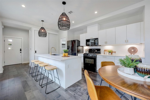 kitchen with a center island with sink, black appliances, decorative light fixtures, white cabinets, and light wood-type flooring