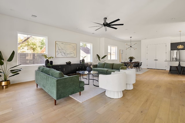 living room with ceiling fan with notable chandelier, a healthy amount of sunlight, and light hardwood / wood-style flooring