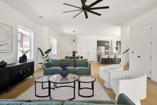 living room with ceiling fan with notable chandelier and light wood-type flooring