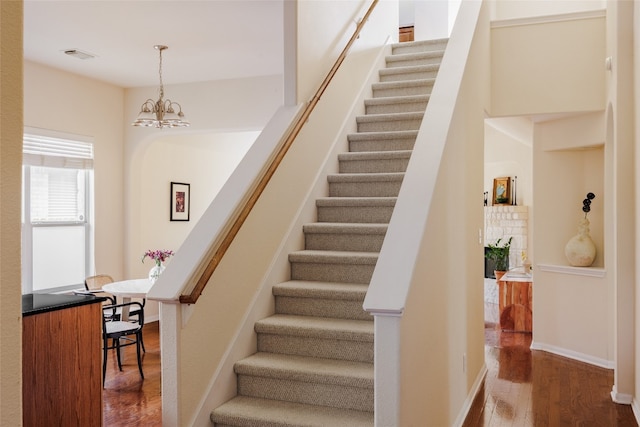 stairs with wood-type flooring and a chandelier