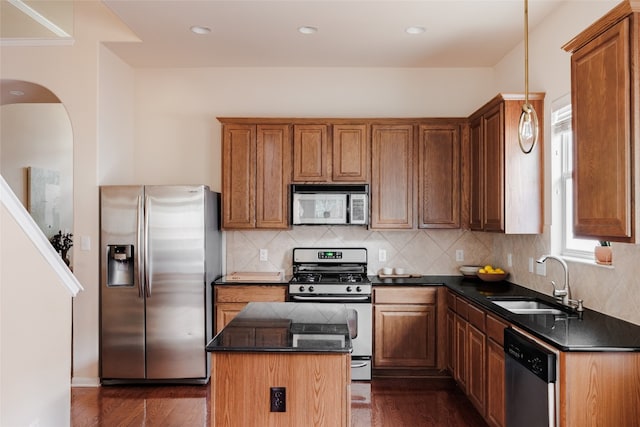 kitchen with appliances with stainless steel finishes, decorative light fixtures, sink, dark wood-type flooring, and a center island