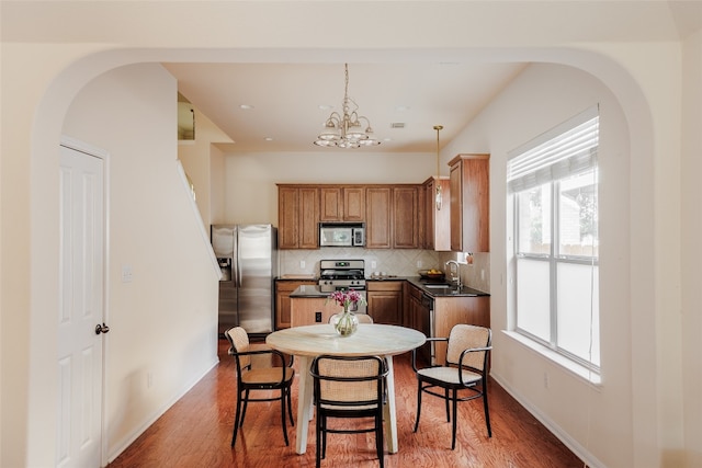 kitchen with hardwood / wood-style flooring, appliances with stainless steel finishes, tasteful backsplash, hanging light fixtures, and a chandelier