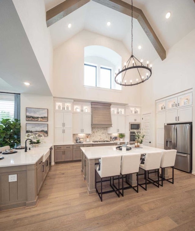 kitchen featuring stainless steel appliances, light hardwood / wood-style floors, custom range hood, decorative light fixtures, and white cabinets