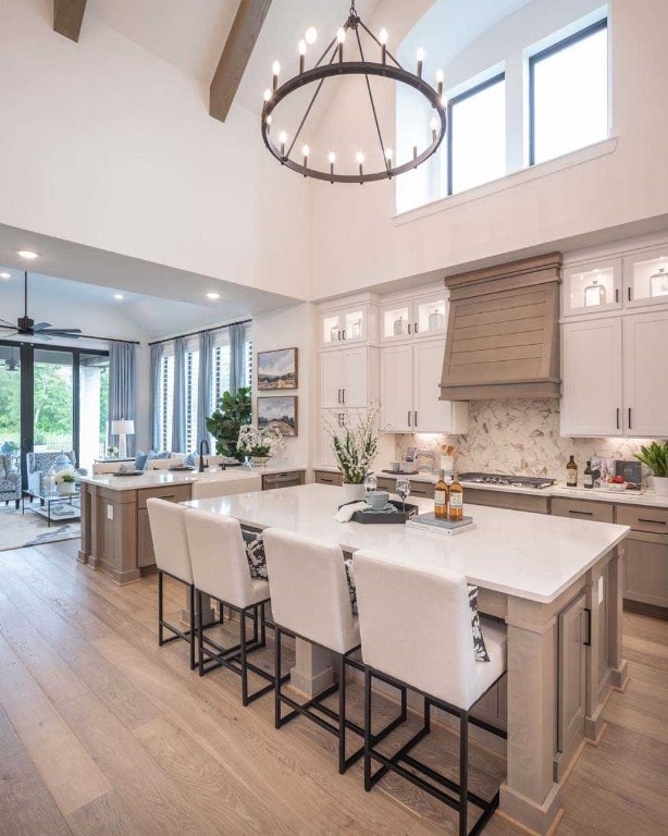 kitchen with light hardwood / wood-style floors, a breakfast bar area, custom exhaust hood, a towering ceiling, and a spacious island