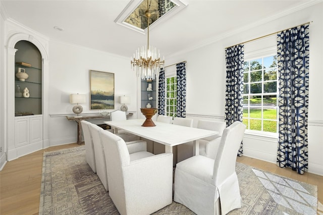 dining space with crown molding, light wood-type flooring, built in shelves, and a notable chandelier