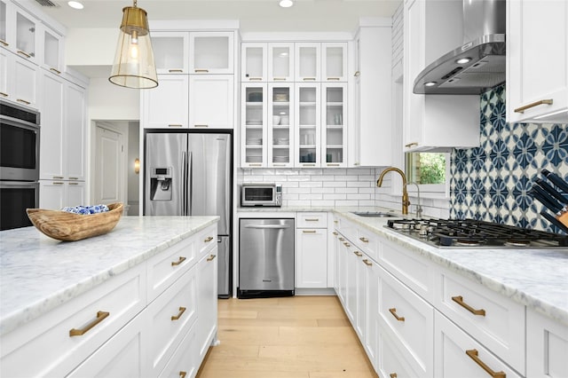 kitchen with white cabinets, hanging light fixtures, wall chimney range hood, light wood-type flooring, and appliances with stainless steel finishes