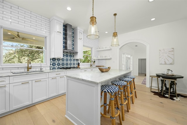 kitchen with light hardwood / wood-style floors, sink, wall chimney exhaust hood, a center island, and white cabinets