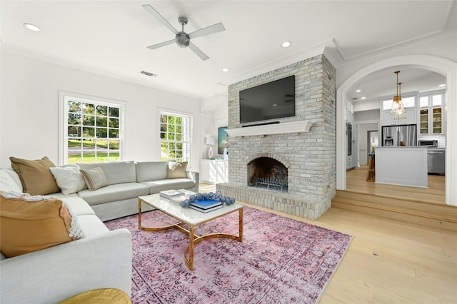 living room featuring a fireplace, light hardwood / wood-style floors, ceiling fan, and crown molding