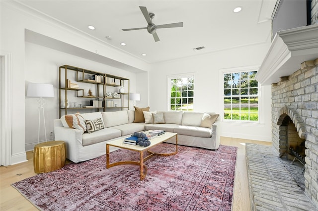 living room featuring ornamental molding, light wood-type flooring, ceiling fan, and a fireplace