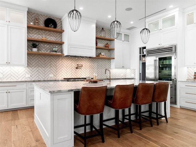 kitchen with light stone counters, a center island with sink, white cabinets, and light hardwood / wood-style flooring