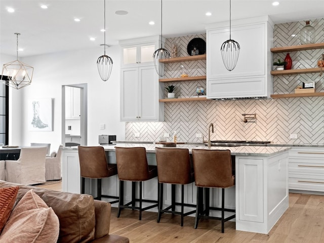 kitchen featuring white cabinetry, hanging light fixtures, a kitchen breakfast bar, a center island with sink, and light wood-type flooring