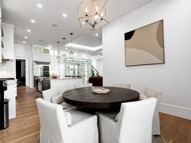 dining area featuring a raised ceiling, light hardwood / wood-style flooring, and an inviting chandelier