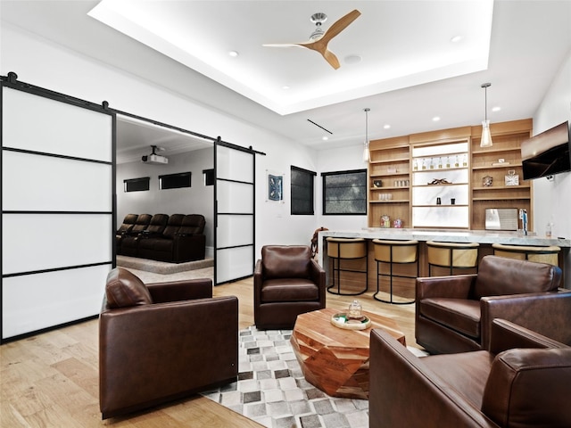 living room featuring a barn door, a tray ceiling, light hardwood / wood-style flooring, and ceiling fan