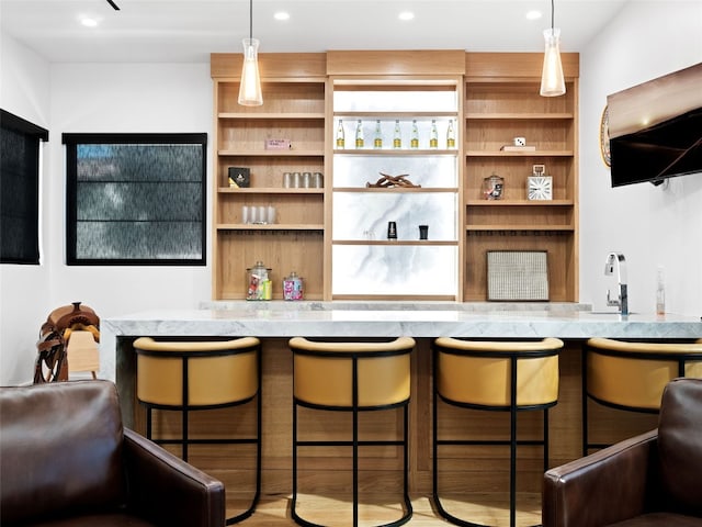 bar featuring light stone counters, sink, hardwood / wood-style floors, and decorative light fixtures