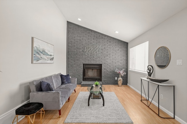 living room with a brick fireplace, light hardwood / wood-style flooring, brick wall, and vaulted ceiling