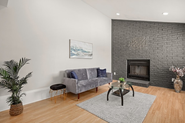 living room with hardwood / wood-style floors, brick wall, vaulted ceiling, and a brick fireplace