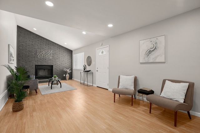 living area featuring a brick fireplace, light wood-type flooring, and vaulted ceiling