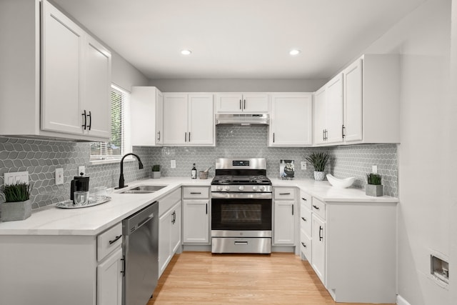 kitchen with stainless steel appliances, white cabinetry, sink, and backsplash