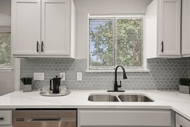 kitchen with white cabinetry, stainless steel dishwasher, sink, and light stone counters