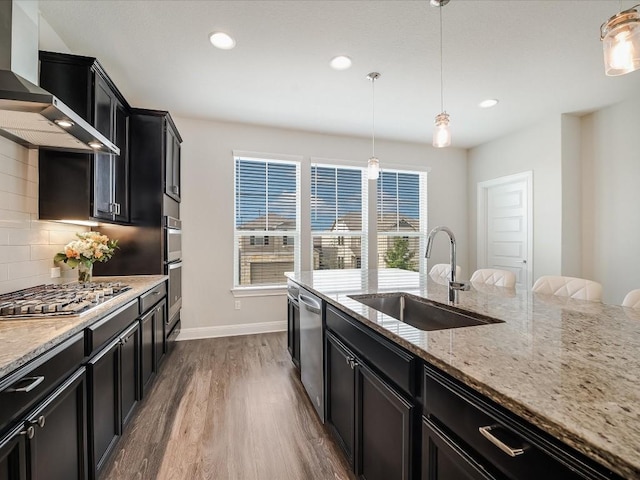 kitchen featuring decorative backsplash, wall chimney exhaust hood, appliances with stainless steel finishes, dark cabinets, and a sink