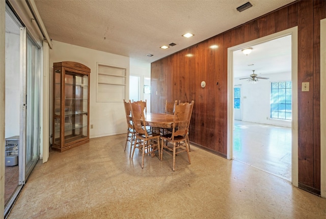 dining space with built in features, ceiling fan, a textured ceiling, and wooden walls