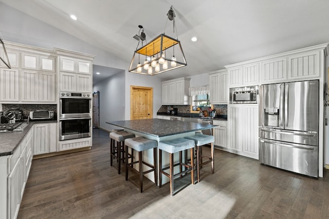 kitchen featuring stainless steel appliances, decorative light fixtures, dark hardwood / wood-style flooring, vaulted ceiling, and a center island