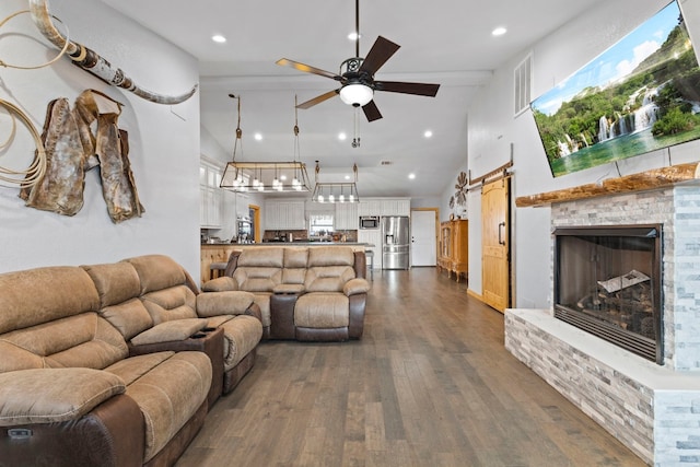 living room featuring a barn door, dark hardwood / wood-style floors, a brick fireplace, lofted ceiling, and ceiling fan