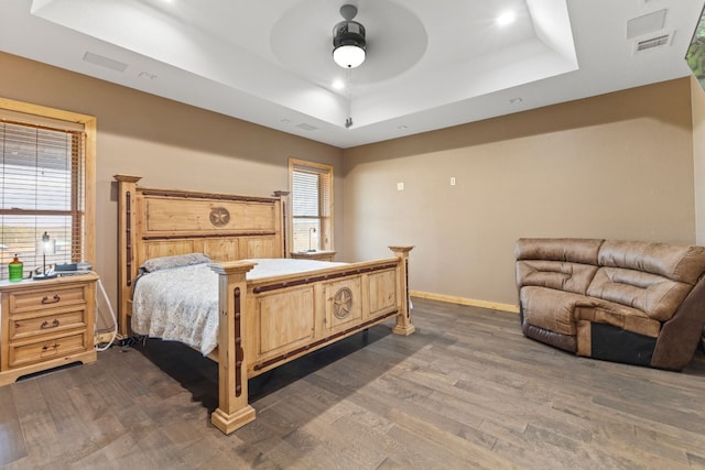 bedroom with hardwood / wood-style floors, multiple windows, a raised ceiling, and ceiling fan