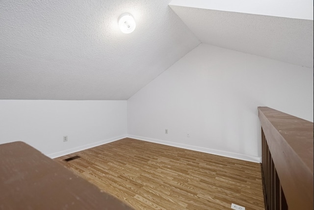 additional living space with hardwood / wood-style flooring, a textured ceiling, and vaulted ceiling