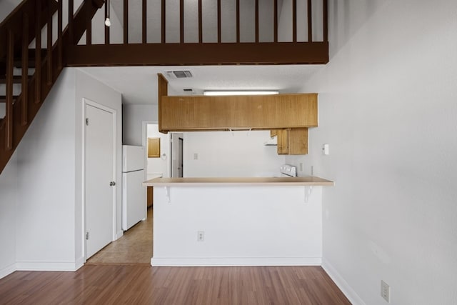 kitchen with white fridge, light hardwood / wood-style flooring, and kitchen peninsula