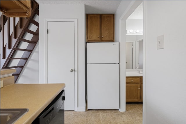 kitchen featuring a textured ceiling, light tile patterned floors, white refrigerator, and dishwasher