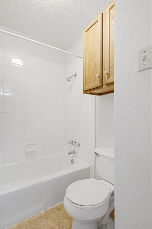 bathroom with a textured ceiling, tile patterned floors, tiled shower / bath, and toilet