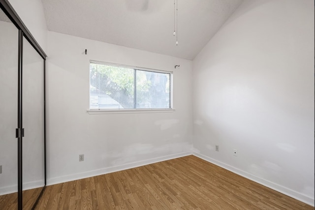 unfurnished bedroom with hardwood / wood-style flooring, vaulted ceiling, and a closet