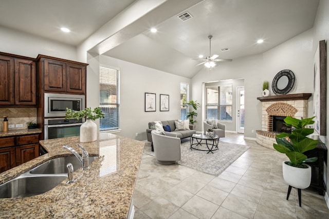 kitchen with a brick fireplace, light stone counters, sink, backsplash, and appliances with stainless steel finishes