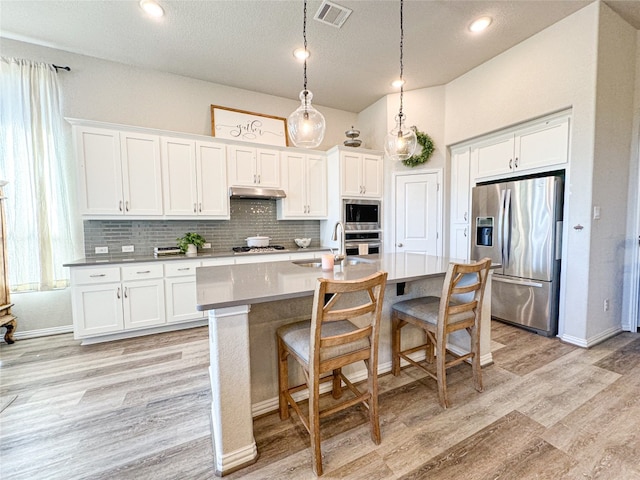 kitchen featuring white cabinetry, light hardwood / wood-style floors, stainless steel appliances, and a center island with sink