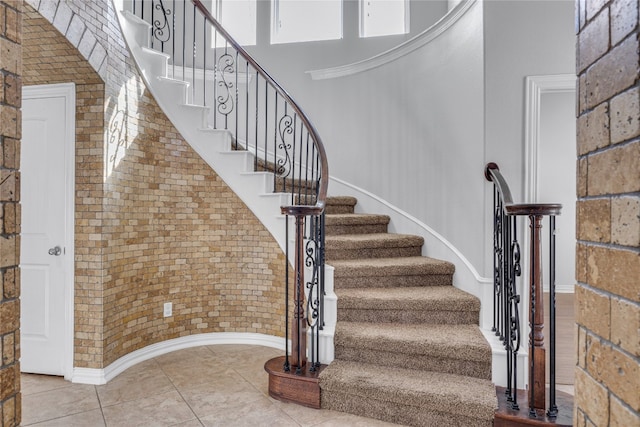 staircase featuring a high ceiling, tile patterned flooring, and brick wall