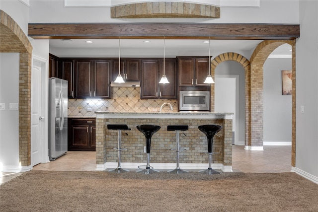 kitchen featuring light tile patterned flooring, stainless steel appliances, decorative light fixtures, a breakfast bar area, and beamed ceiling