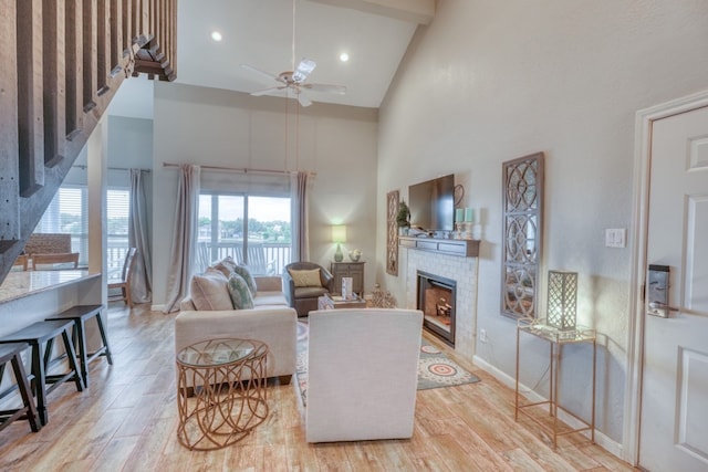 living room with ceiling fan, a tile fireplace, light wood-type flooring, and high vaulted ceiling