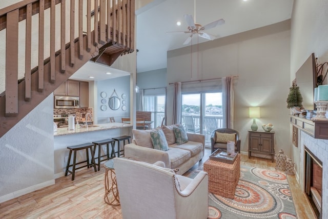 living room featuring light hardwood / wood-style floors, ceiling fan, sink, and high vaulted ceiling