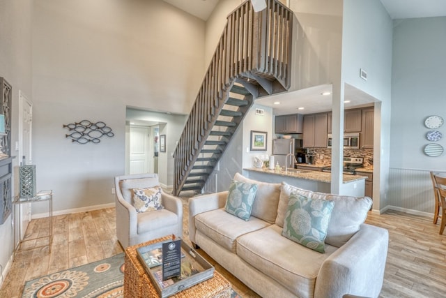 living room featuring a high ceiling, sink, and light hardwood / wood-style flooring