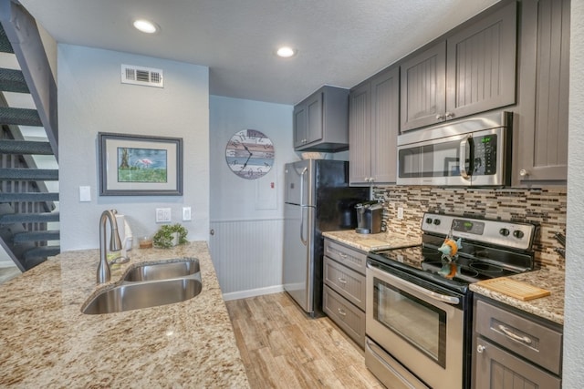 kitchen with stainless steel appliances, sink, light hardwood / wood-style flooring, and light stone counters