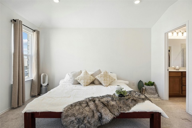 bedroom featuring lofted ceiling, light carpet, and ensuite bath