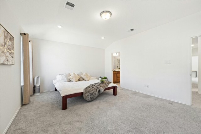 carpeted bedroom with ensuite bathroom and vaulted ceiling