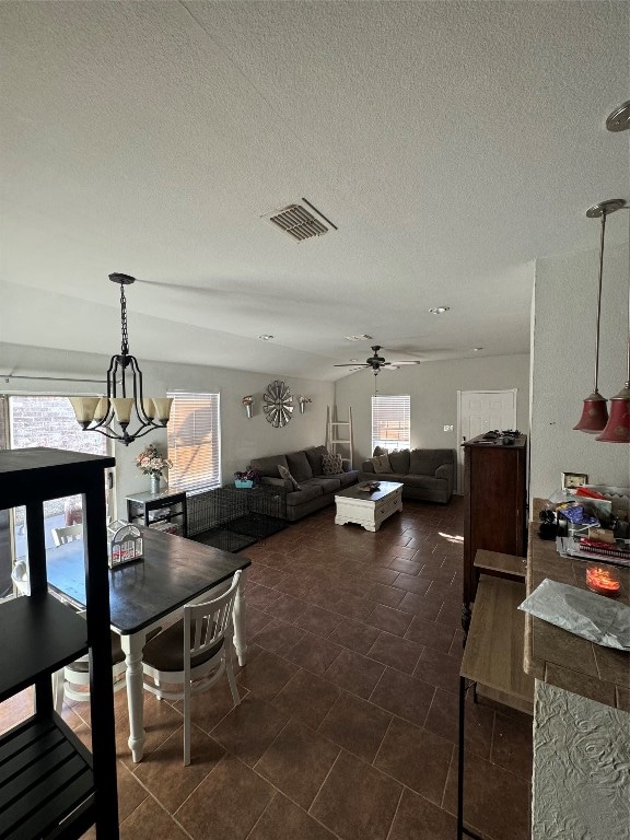 dining space featuring ceiling fan with notable chandelier, a healthy amount of sunlight, and a textured ceiling