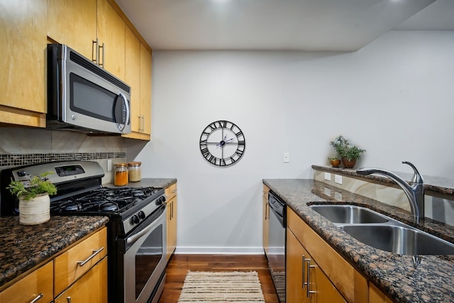 kitchen with dark wood-type flooring, sink, dark stone counters, and appliances with stainless steel finishes