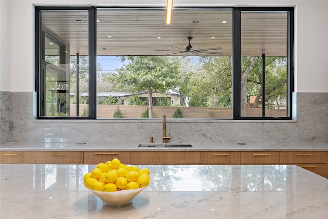 interior space featuring decorative backsplash, ceiling fan, light stone counters, and sink